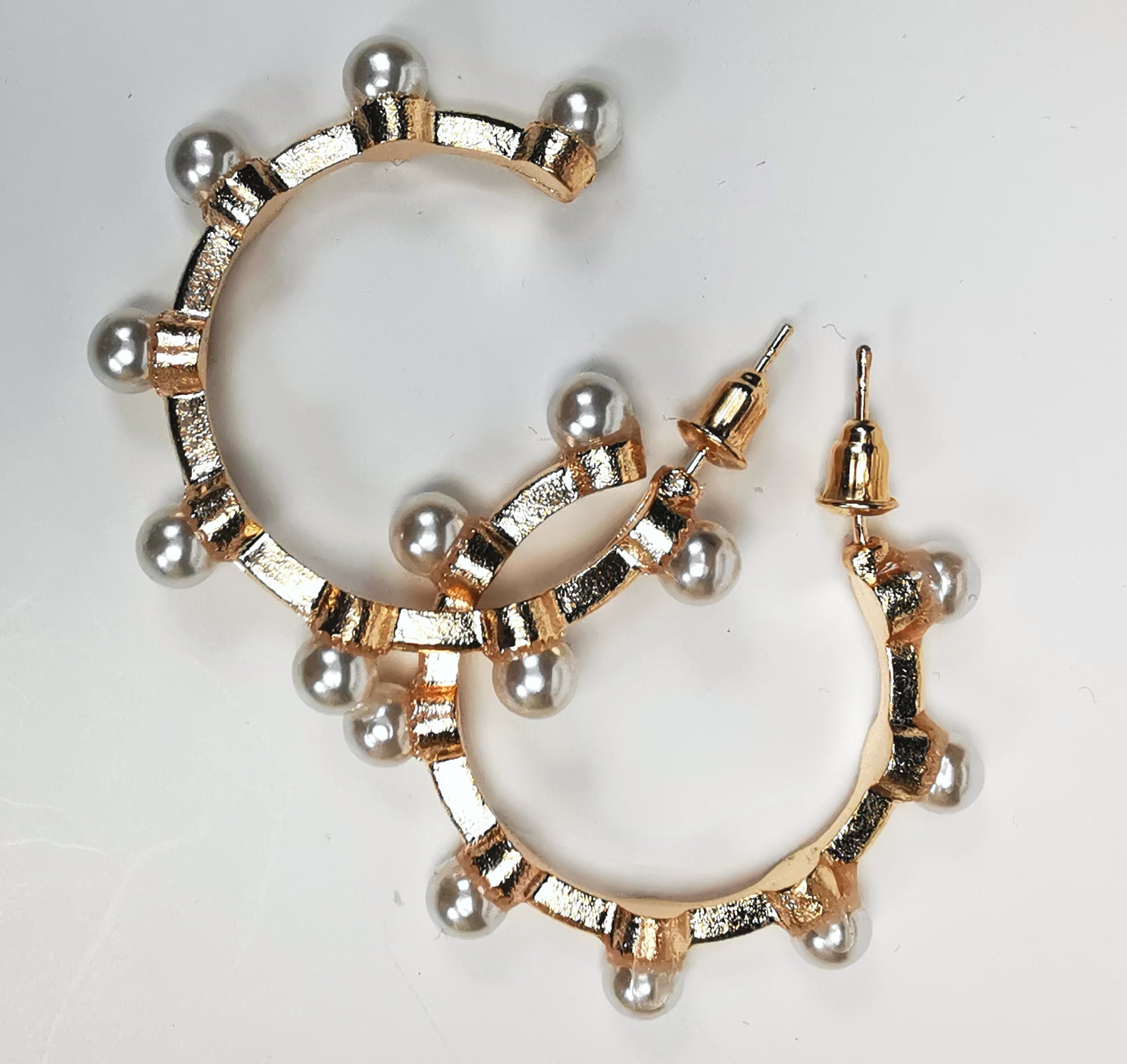 Boucles d'oreilles créoles fantaisie, en alliage doré, 35mm de diamètre, sur clous, avec 8 perles fantaisie sur la périphérie. Présentées l'une à coté de l'autre, posées sur fond blanc. Vue de dessus en gros plan.