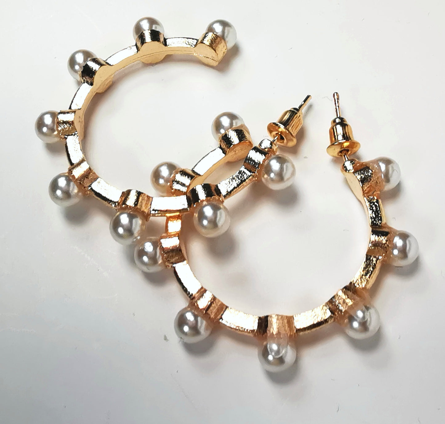Boucles d'oreilles créoles fantaisie, en alliage doré, 35mm de diamètre, sur clous, avec 8 perles fantaisie sur la périphérie. Présentées l'une à coté de l'autre, posées sur fond blanc. Vue de dessus.