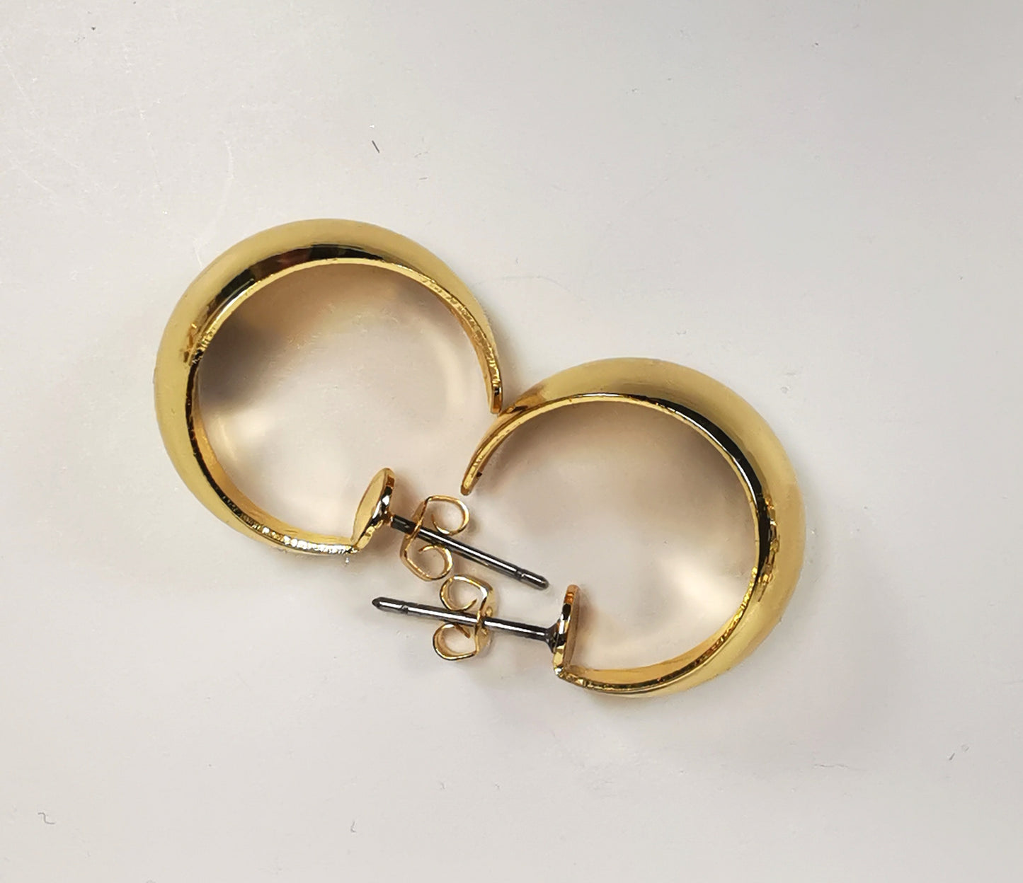 Boucles d'oreilles créoles larges dorées, 20mm de diamètre, 12mm de large, sur clous, Présentées posées l'une à coté de l'autre en sens inverse , vue de dessus en gros plan.