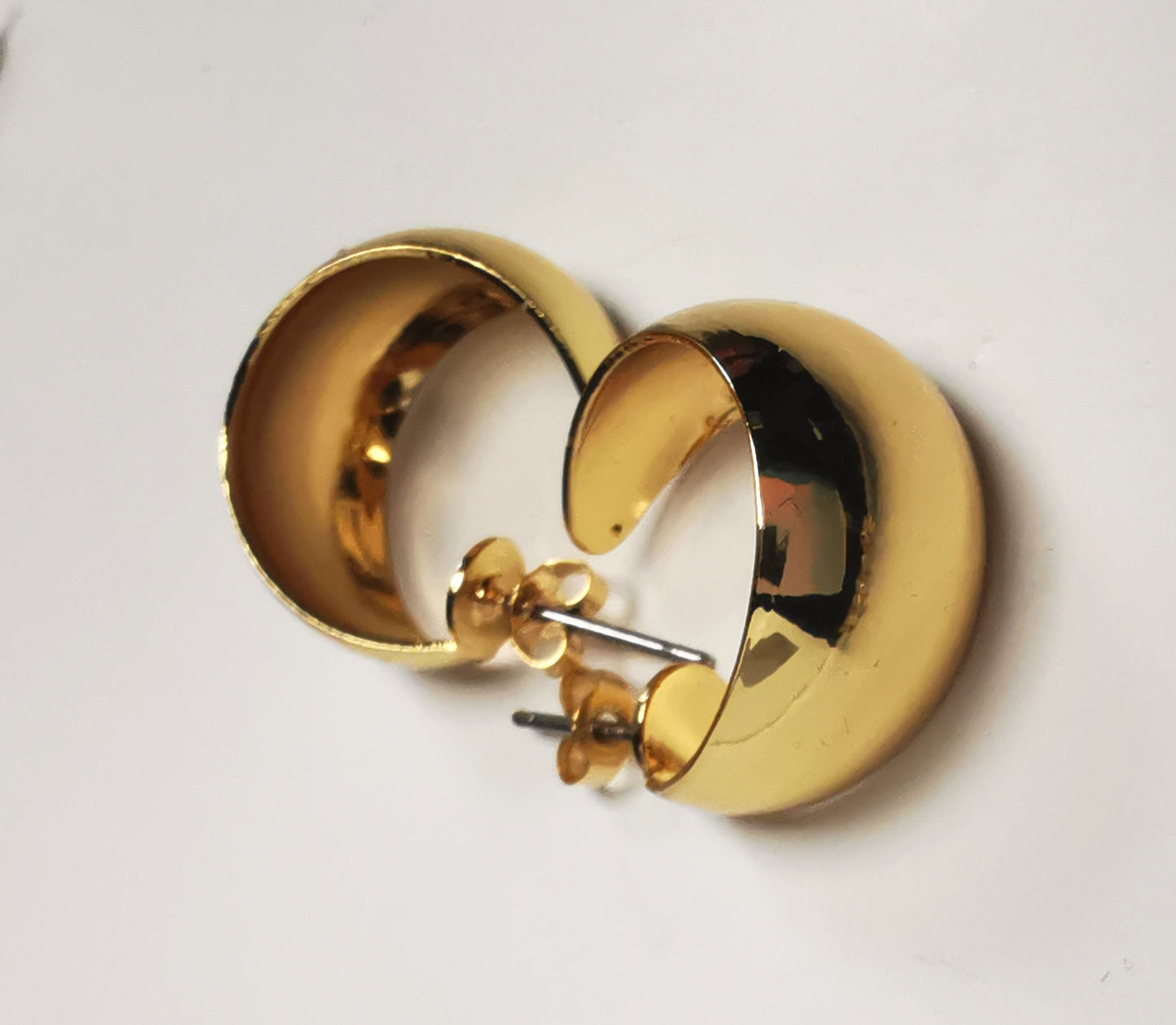 Boucles d'oreilles créoles larges dorées, 20mm de diamètre, 12mm de large, sur clous, Présentées posées l'une à coté de l'autre en sens inverse , vue de droite en gros plan.