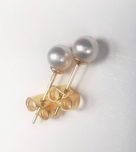 Boucles d'oreilles perles de culture blanches rondes 5mm montées sur clous plaqués or. Présentées cote à cote, perles en haut, les deux décalées vers la droite, sur fond blanc. Vue de dessus en très gros plan.